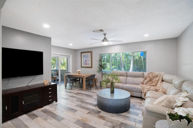 living room featuring ceiling fan, visible vents, light wood finished floors, and a textured ceiling