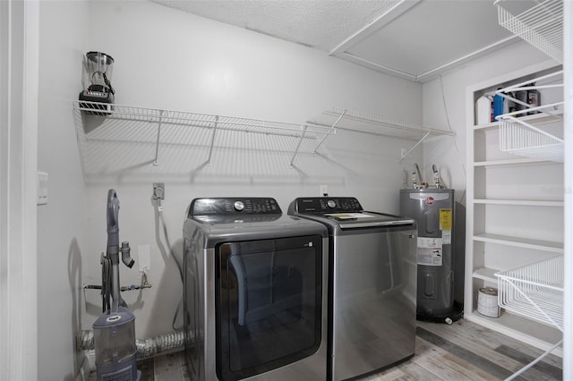 clothes washing area with washing machine and clothes dryer, water heater, laundry area, wood finished floors, and a textured ceiling