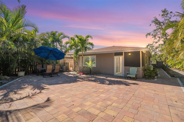 patio terrace at dusk featuring a ceiling fan, central air condition unit, outdoor dining area, and fence