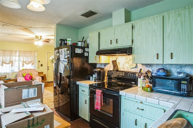 kitchen with visible vents, tile patterned flooring, black appliances, tile counters, and under cabinet range hood