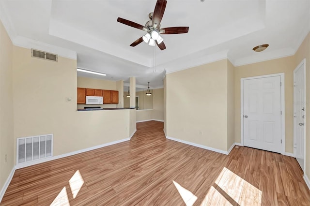 unfurnished living room featuring visible vents, light wood-style flooring, and a raised ceiling