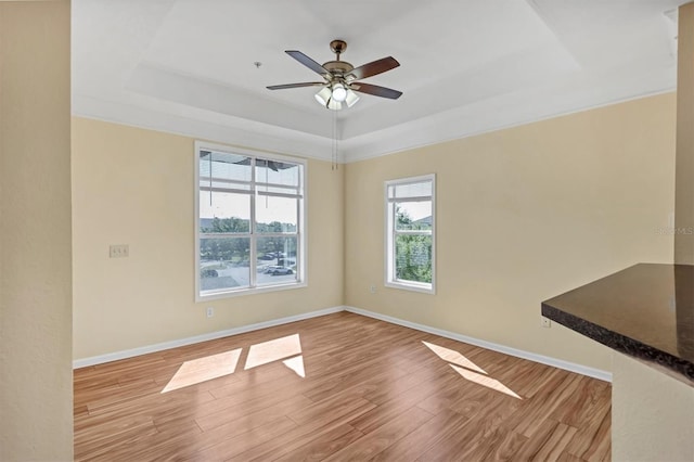 interior space with baseboards, a raised ceiling, light wood-style floors, and a ceiling fan