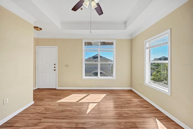 empty room with a tray ceiling, baseboards, and wood finished floors