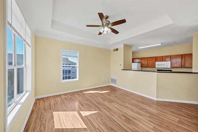 unfurnished living room featuring visible vents, light wood-type flooring, and a tray ceiling