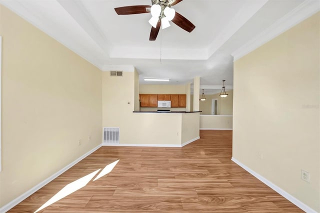 unfurnished living room with light wood finished floors, visible vents, ceiling fan, baseboards, and a tray ceiling