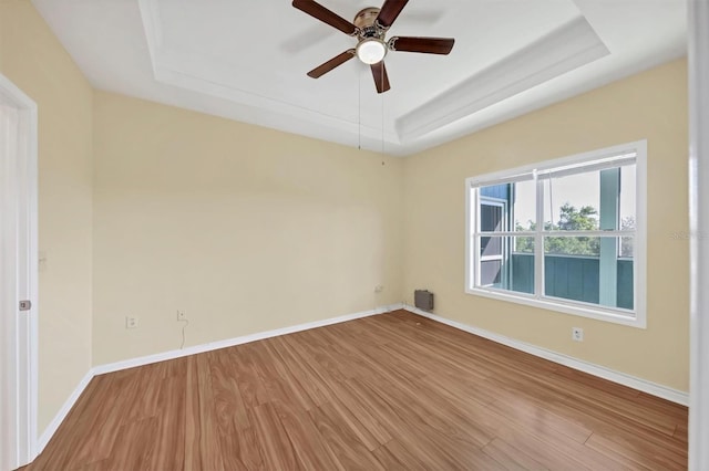 empty room featuring ceiling fan, a tray ceiling, baseboards, and wood finished floors