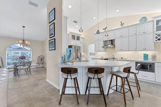 kitchen featuring wall chimney range hood, a breakfast bar area, visible vents, and appliances with stainless steel finishes