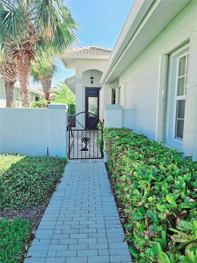 view of exterior entry with a tiled roof, stucco siding, fence, and a gate