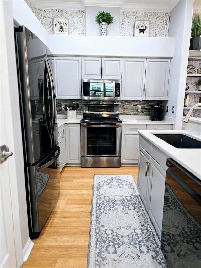 kitchen with ornamental molding, a sink, black appliances, light countertops, and light wood-type flooring