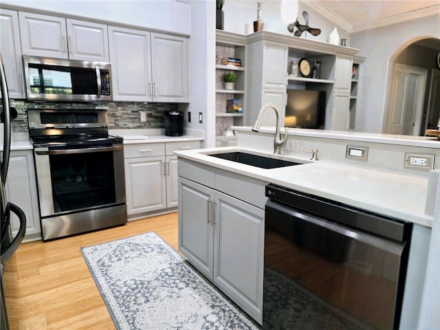 kitchen featuring a sink, stainless steel appliances, light countertops, crown molding, and tasteful backsplash