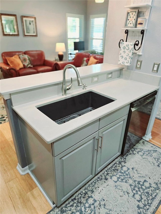 kitchen featuring light wood-type flooring, light countertops, black dishwasher, and a sink