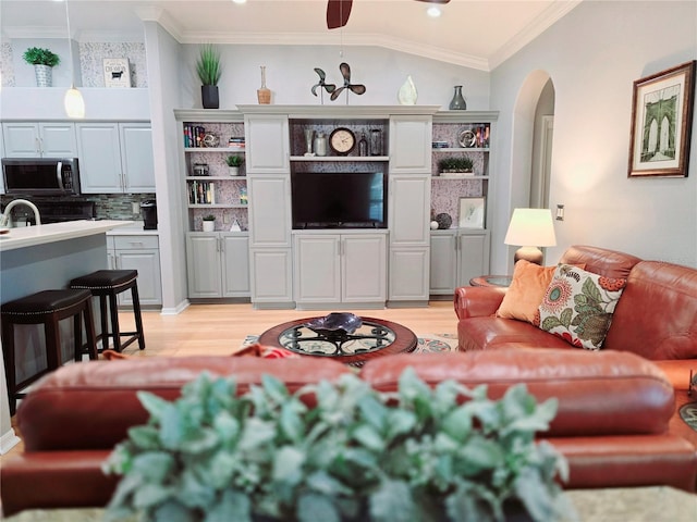 living area with arched walkways, light wood-style floors, and ornamental molding