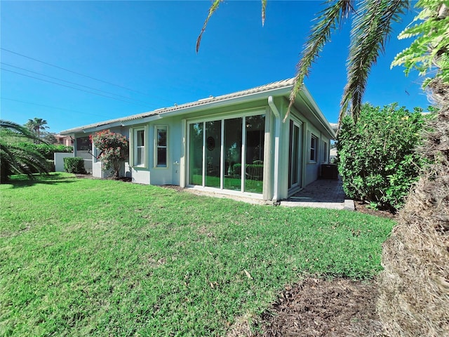 rear view of house featuring a lawn, a sunroom, and stucco siding