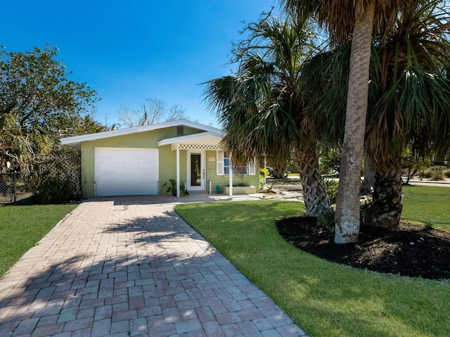 view of front facade featuring stucco siding, decorative driveway, fence, a front yard, and a garage