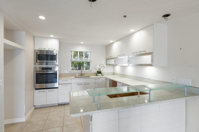 kitchen featuring a sink, white cabinetry, stainless steel appliances, a peninsula, and light tile patterned flooring