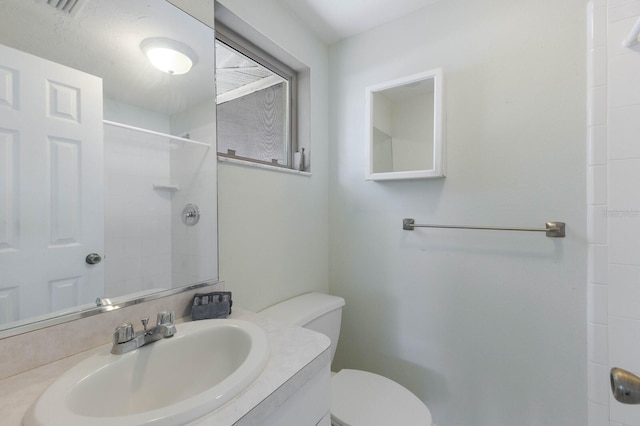 bathroom featuring toilet, vanity, and a tile shower