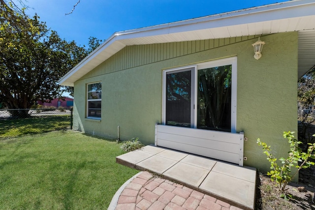 view of side of property featuring stucco siding, a lawn, and fence