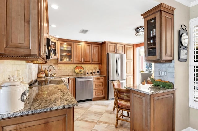 kitchen featuring brown cabinets, a sink, stainless steel appliances, glass insert cabinets, and light stone countertops