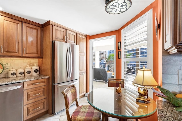 kitchen with backsplash, light stone countertops, light tile patterned floors, brown cabinetry, and stainless steel appliances