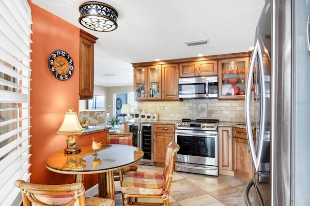 kitchen featuring tasteful backsplash, light stone countertops, wine cooler, brown cabinets, and stainless steel appliances