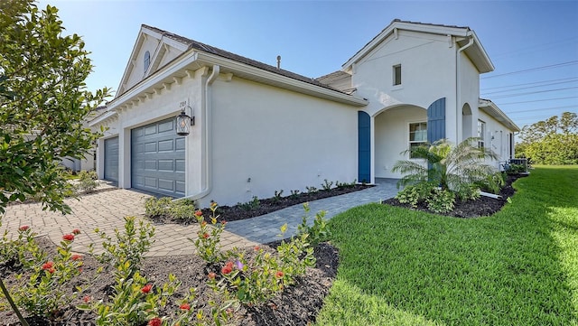 view of front of property featuring stucco siding, decorative driveway, a garage, and a front lawn
