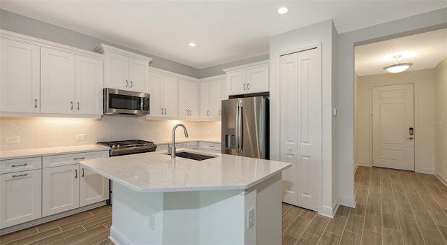 kitchen with backsplash, wood finish floors, appliances with stainless steel finishes, white cabinets, and a sink
