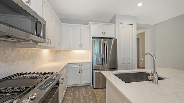 kitchen with tasteful backsplash, light stone countertops, stainless steel appliances, white cabinetry, and a sink