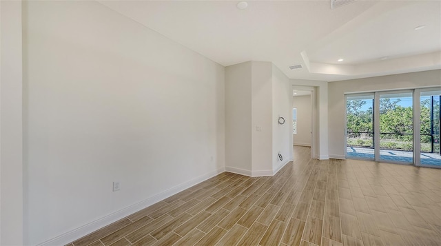 unfurnished room featuring light wood finished floors, visible vents, baseboards, recessed lighting, and a raised ceiling
