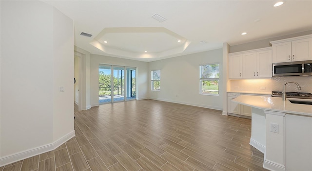 kitchen featuring visible vents, stainless steel microwave, light countertops, decorative backsplash, and a raised ceiling