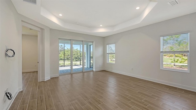empty room with a raised ceiling, wood finished floors, visible vents, and baseboards