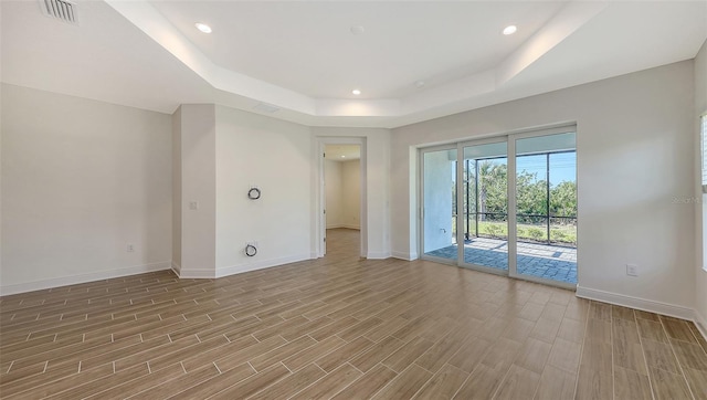 empty room with a raised ceiling, wood finished floors, baseboards, and visible vents