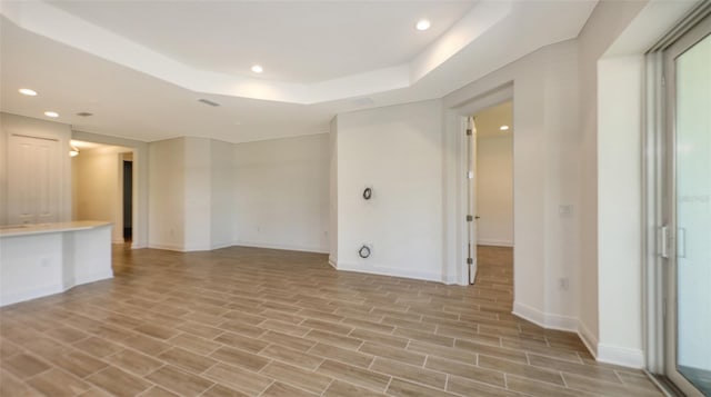 spare room with recessed lighting, baseboards, a raised ceiling, and light wood finished floors