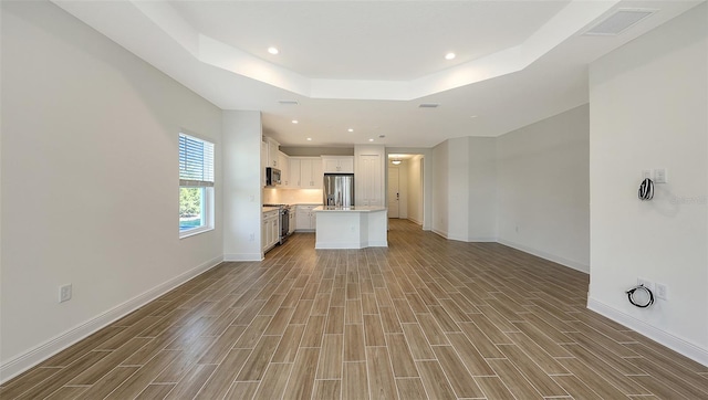 unfurnished living room featuring visible vents, recessed lighting, baseboards, a raised ceiling, and wood tiled floor