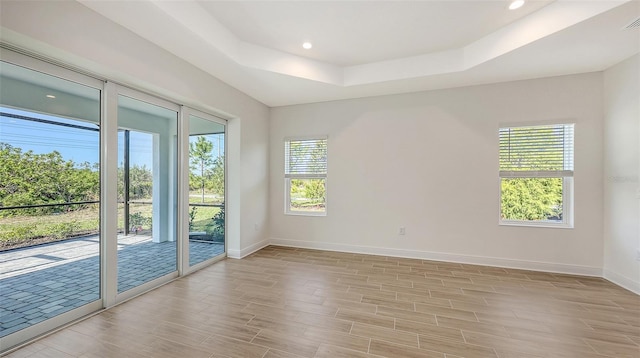 empty room featuring recessed lighting, a tray ceiling, baseboards, and light wood finished floors