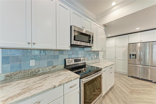 kitchen with tasteful backsplash, white cabinets, appliances with stainless steel finishes, and crown molding