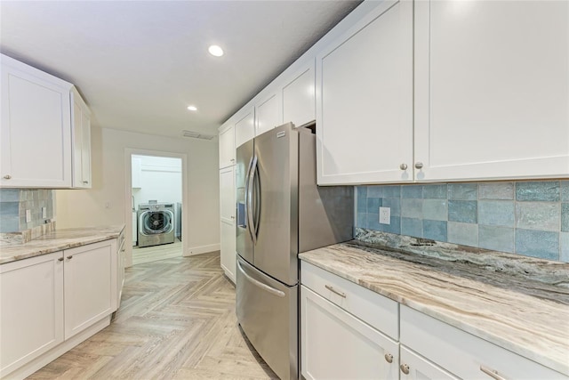 kitchen featuring washing machine and clothes dryer, decorative backsplash, stainless steel fridge, and white cabinetry