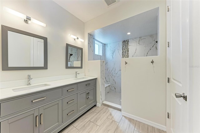 full bath with double vanity, baseboards, a marble finish shower, and a sink