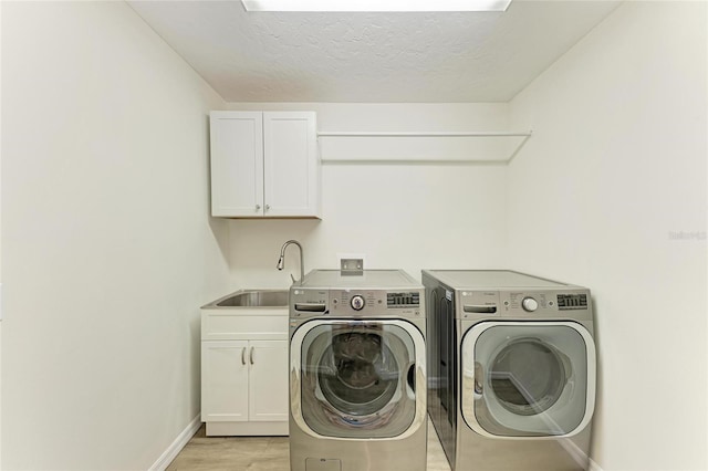 clothes washing area with light wood finished floors, baseboards, washer and clothes dryer, cabinet space, and a sink