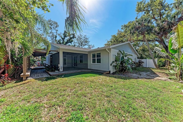 back of house with stucco siding, a lawn, a sunroom, and fence