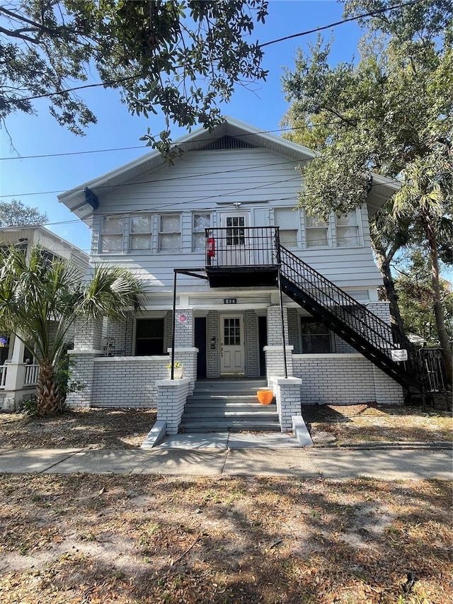 view of front of house featuring brick siding, stairway, and covered porch