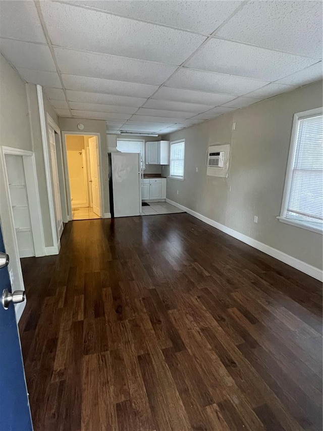 unfurnished living room with a drop ceiling, an AC wall unit, baseboards, and wood finished floors