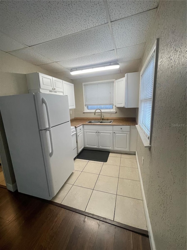 kitchen with freestanding refrigerator, a textured wall, white cabinets, a paneled ceiling, and a sink