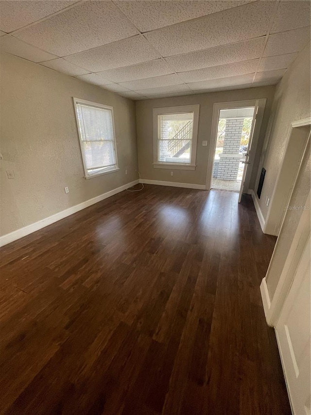 unfurnished living room with a drop ceiling, baseboards, dark wood-type flooring, and a textured wall