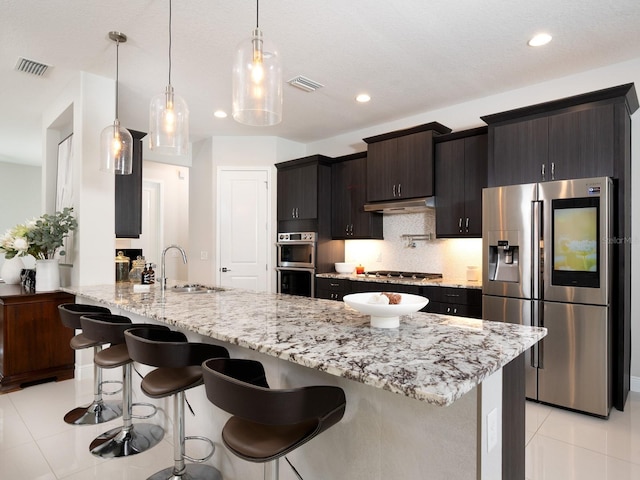 kitchen with visible vents, a sink, under cabinet range hood, tasteful backsplash, and appliances with stainless steel finishes