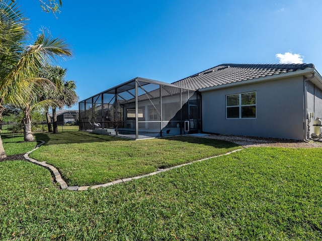 rear view of house featuring a lanai, a tiled roof, a yard, and stucco siding