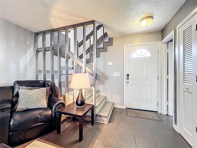 foyer entrance featuring stairway, baseboards, and a textured ceiling