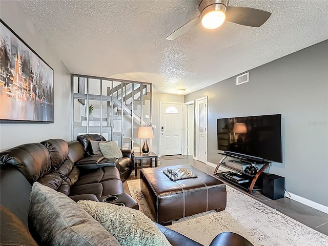 living area featuring baseboards, visible vents, ceiling fan, stairs, and a textured ceiling