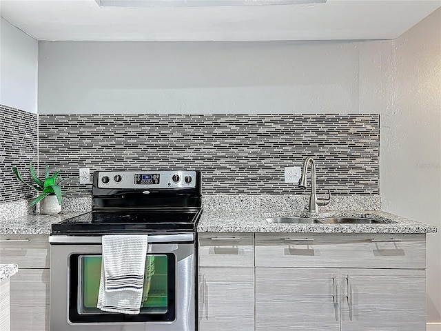 kitchen featuring a sink, decorative backsplash, light stone counters, and stainless steel range with electric stovetop