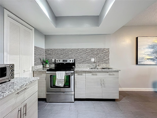 kitchen with a sink, backsplash, baseboards, stainless steel electric range oven, and light stone countertops