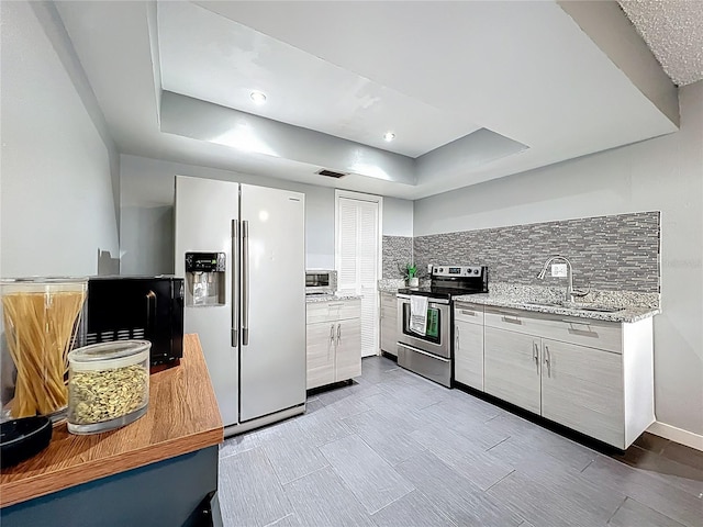 kitchen with electric range, a sink, white refrigerator with ice dispenser, a raised ceiling, and tasteful backsplash